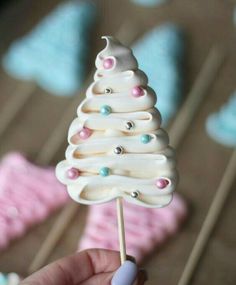 a hand holding a white christmas tree shaped lollipop on a toothpick stick