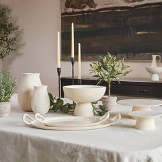 the table is set with white dishes and candles