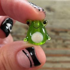 a person holding a tiny green frog in their left hand with black and white designs on it