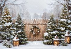 christmas trees and lanterns in front of a wooden fence with wreaths on the gate