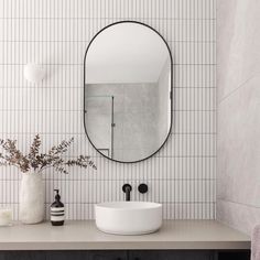 a white sink sitting under a round mirror next to a wall mounted faucet