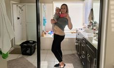 a woman holding a baby in her arms while standing in front of a bathroom mirror