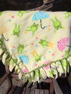 a baby blanket that is on top of a wooden bench with an umbrella and frog print