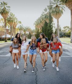 a group of young women walking across a street next to palm tree lined streets in short shorts