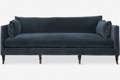 a blue velvet couch with wooden legs and an upholstered back, in front of a white background