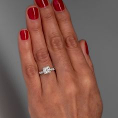 a woman's hand with red nail polish holding an engagement ring on her finger