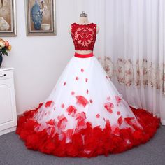 a white and red wedding dress with flowers on the skirt is displayed in front of a window