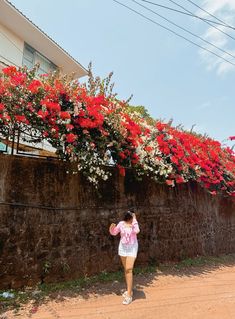 a woman standing in front of a fence with red flowers growing on the side of it