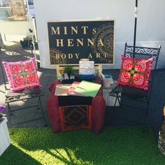 two lawn chairs and a table with decorative pillows on it in front of a sign that reads mint's henna body art