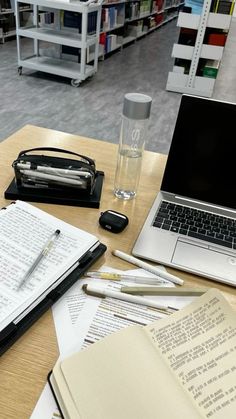 an open laptop computer sitting on top of a wooden table next to books and papers