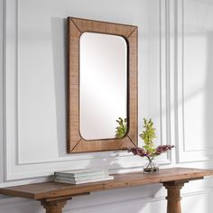 a wooden table topped with a vase filled with flowers and a mirror on top of it