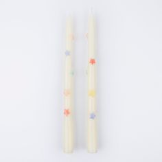 two white candles with multicolored stars sitting next to each other on a white surface