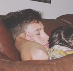 a young boy and girl cuddle on a brown leather couch in the living room