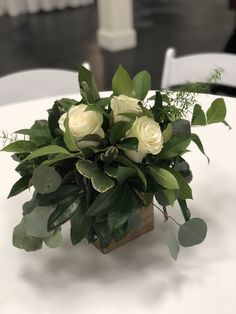 a vase filled with white roses and greenery on top of a dining room table