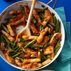 a white bowl filled with chicken and asparagus on top of a blue table