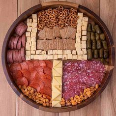 a wooden platter filled with different types of meats, cheese and crackers