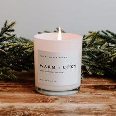 a white candle sitting on top of a wooden table next to evergreen branches and pine cones