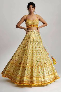 To further enhance its beauty, the ashi lehenga is adorned with pompoms and tassels. These playful elements add a whimsical touch and create a sense of movement as you glide across the dance floor. The pompoms and tassels are meticulously crafted and delicately attached, ensuring they stay in place throughout your glamorous wedding ceremony. Bohemian Sharara With Gota Work For Reception, Festive Sharara With Tassels And Traditional Drape, Festive Traditional Drape Sharara With Tassels, Navratri Anarkali Dress With Tassels, Anarkali Dress With Tassels For Navratri, Yellow Embellished Dress For Navratri, Festive Sharara With Tassels For Reception, Yellow Embellished Traditional Wear For Festive Occasions, Diwali Anarkali Set With Tassels And Traditional Drape