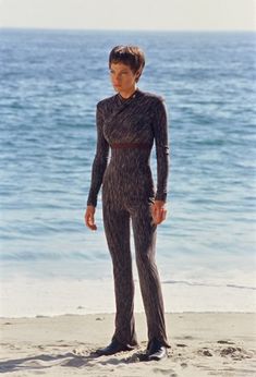 a woman standing on top of a sandy beach next to the ocean wearing a wet suit