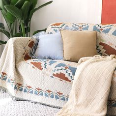 a couch covered in blankets and pillows next to a potted plant