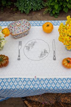 a place mat with flowers and fruit on it, sitting next to a bowl of oranges