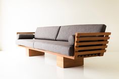 a couch made out of wood and grey fabric sitting on top of a white floor