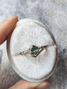 someone is holding an engagement ring with a green stone