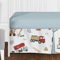 a baby bed with construction trucks and dump trucks on it's cover, next to a chair