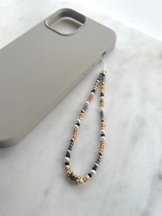 a cell phone and beaded necklace on a marble table next to a gray case