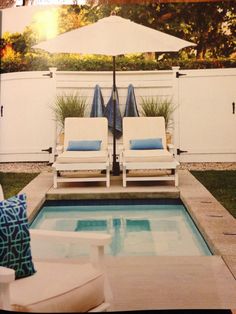 two lawn chairs sitting next to a swimming pool with an umbrella over it and blue pillows