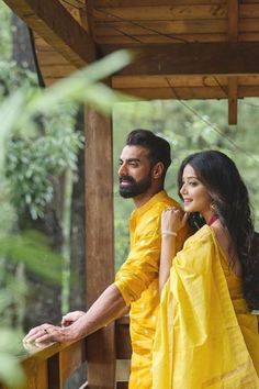 a man and woman dressed in yellow posing for a photo together on a porch with trees in the background