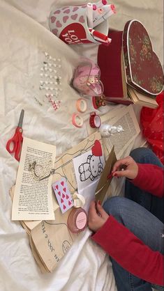 a woman sitting on top of a bed next to an open book and sewing supplies