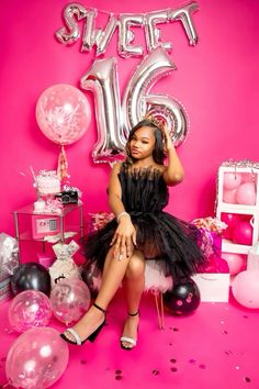 a woman in a black dress sitting on a pink floor with balloons and streamers