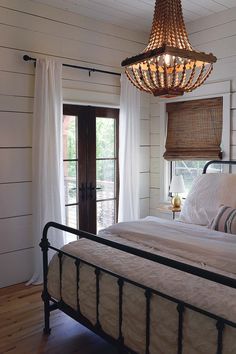 a bedroom with white walls and wood flooring has a chandelier hanging from the ceiling