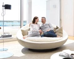 a man and woman sitting on a bean bag chair in front of a large window