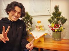 a young man is making the peace sign with his fingers while sitting in front of some potted plants