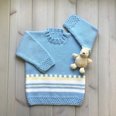 a knitted sweater with a teddy bear on the front and bottom, sitting next to it