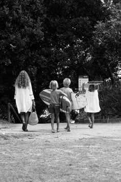 three women carrying surfboards and walking towards the beach with trees in the back ground