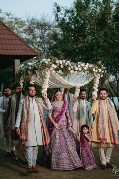 a group of people standing next to each other in front of a gazebo with flowers on it