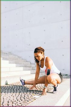 a woman squatting down on the ground in front of some stairs with her leg up