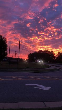 the sun is setting over an intersection with street lights and trees in the foreground