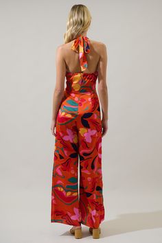 Throw on your favorite sandals and celebrate summer in the Serene Floral Magic Moment Halter Jumpsuit! A halter design features a surplice neckline. A wide waistband tops pleated wide leg pants with side slits to show off a little side leg. Don’t forget gold accessories for a completed look.- Satin- Halter- Button snap- Wide leg slits- Color: Orange MulSize + Fit - Model is 5'11" and wearing size XS- Measurements taken from size S - Waist: 27"- Inseam: 2 1/4" Fabric Self: 100% Polyester Lining: Summer Party V-neck Halter Top, V-neck Halter Top For Summer Parties, Summer Evening Halter Neck Jumpsuits And Rompers, Summer Evening Jumpsuits And Rompers With Halter Neck, Summer Fitted Halter Neck Jumpsuits And Rompers, Summer Evening Jumpsuit With Tie Back, Summer Evening Jumpsuits And Rompers With Tie Back, Fitted Halter Neck Summer Jumpsuits And Rompers, Chic Strapless V-neck Jumpsuit For Summer