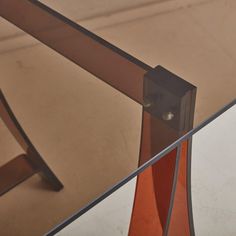 an orange vase sitting on top of a glass table next to a metal frame and mirror