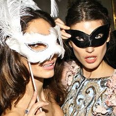 two women with masks on their faces posing for the camera at a masquerade party