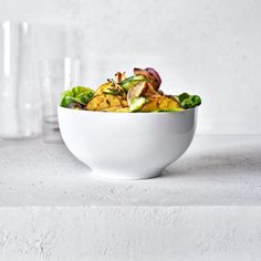 a white bowl filled with food next to two glasses on a counter top in front of a wall