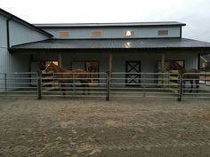 two horses standing in an enclosed area next to a building with metal roof and windows