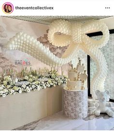 a cake and flowers on a table in front of a wall with balloons hanging from it