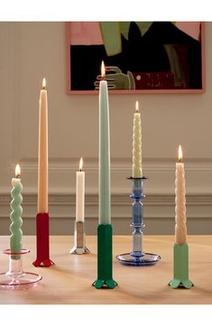 candles are arranged in different colors and sizes on a table with a painting behind them