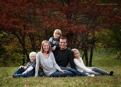 a family sitting on the grass in front of some trees