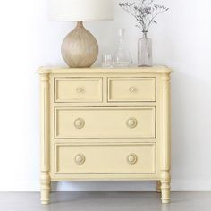 a white dresser sitting next to a lamp on top of a table